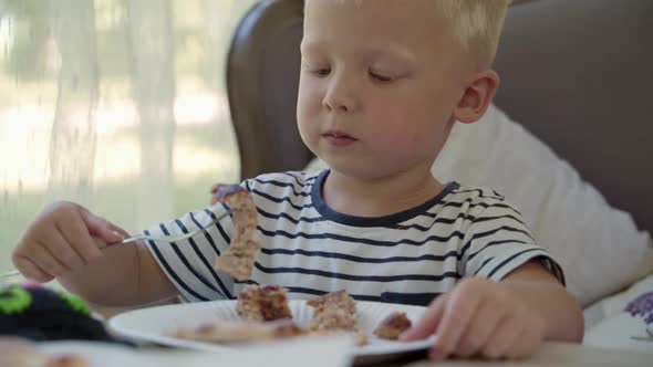 A little boy sits at a table in a cafe and eats a delicious pie.