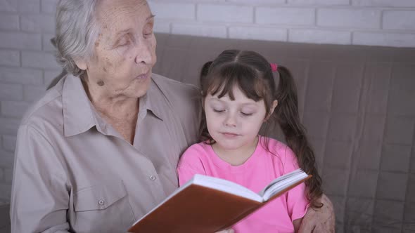 An elderly woman reads a book to a child. 