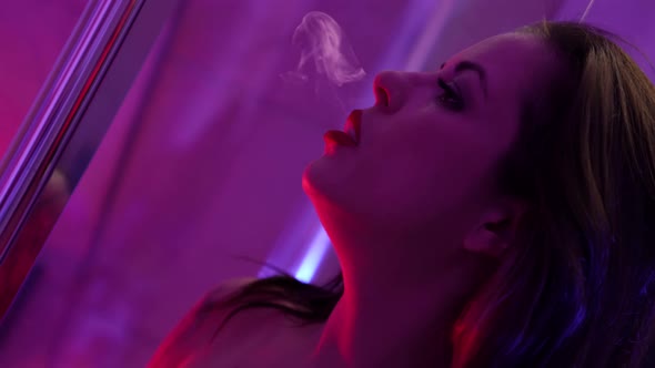Sexy Lady is Smoking Ecigarette Indoors at Night Breathing Smoke Closeup Portrait