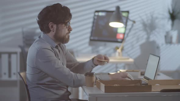 Man Working in Office in Evening and Eating Pizza