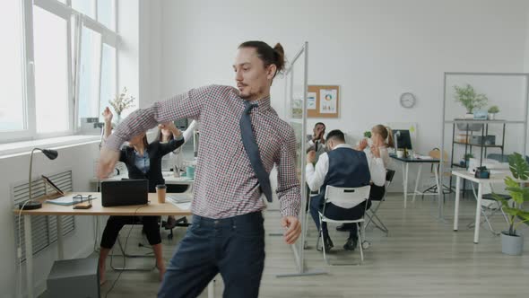 Young Dancer in Formal Clothing Moving to Music in Workplace While Colleagues Dancing in Background