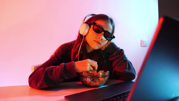Girl in Glasses for 3D and Headphones Watches Sad Movie on Laptop Eats Popcorn