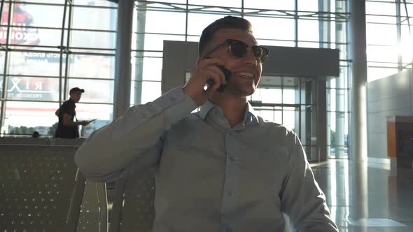 Young Smiling Businessman Talking on Phone at Airport with Sun Flare at Background