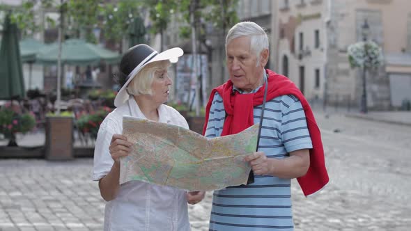 Senior Male and Female Tourists Standing with a Map in Hands Looking for Route