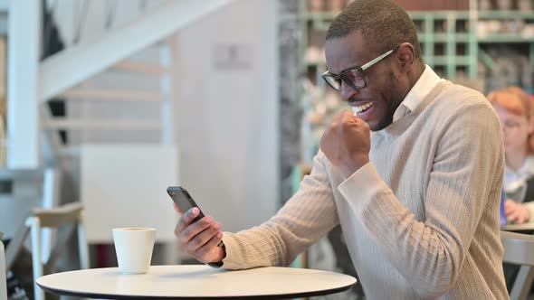 Ambitious African Man Celebrating Success on Smart Phone