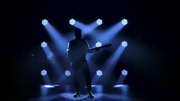 Silhouette of a Young Guy Playing on the Electric Guitar on Stage in a Dark Studio with Smoke and