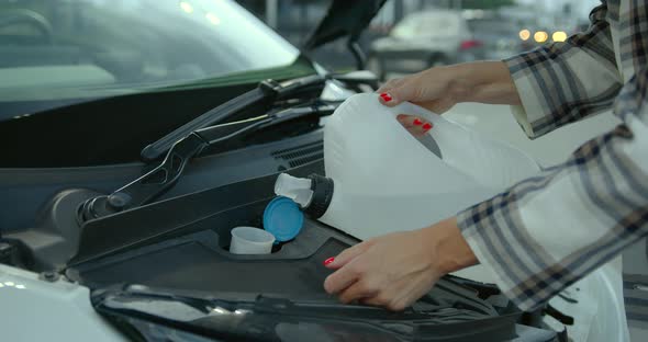 A Woman Pours Antifreeze Into Her Car at a Service Station