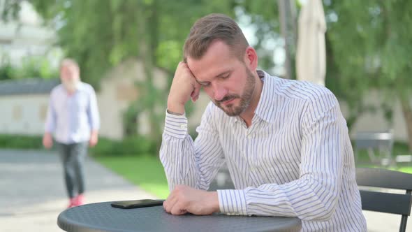 Middle Aged Man Taking Nap While Sitting in Outdoor Cafe