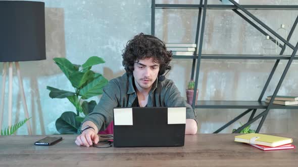 Young Curly Haired Man Using Laptop Computer with Headset to Talking Online