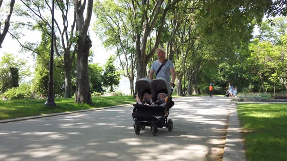 Father with kids in double stroller in a park. Man pushing twins stroller, Pram.