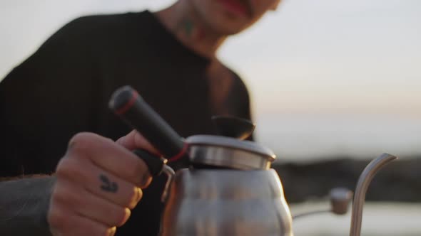 Mustached Guy with Tattoo on His Neck Holding Kettle with Boiled Water on Seashore Slow Motion