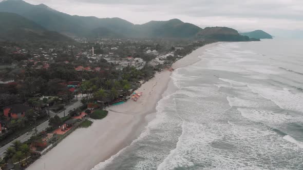 Lateral drone footage of the beach, mountain and houses in front of the sea, cloudy day, waves, land