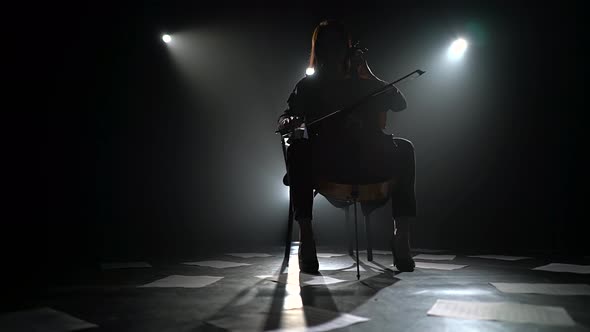 Girl Plays the Composition on the Cello on the Floor Are Scattered Sheets with Notes