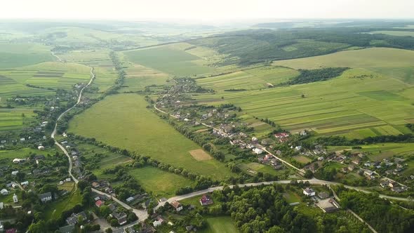 Aerial View of Small Village with Small Houses Among Green Trees with Farm Fields and Distant Forest