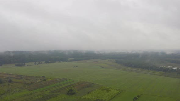 Aerial Hyperlapse, Top View Drone Flies Through Rain Clouds Rolling Over Green Forest and Field