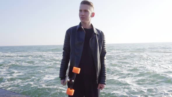 Young Man Holds His Longboard Standing By the Sea