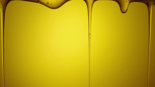 Drops of Thick Golden Honey Flowing Down on a Yellow Background