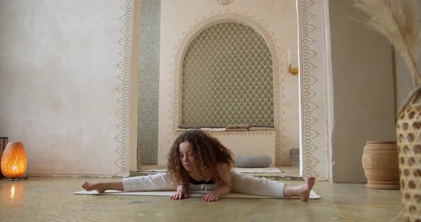 Sporty CurlyHaired Woman Does Yoga Stretching Exercises