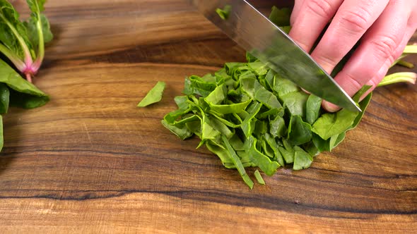 The cook cuts spinach leaves on a wooden cutting board.