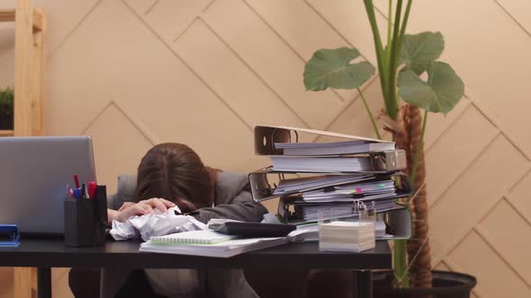 Office Worker Woman Sleeps with Head Down on Table on Which Laptop Crumpled Pieces of Paper Folders