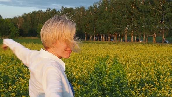 Attractive Young Blonde Woman Walks Through a Field of Rapeseed Smiling and Spinning Merrily