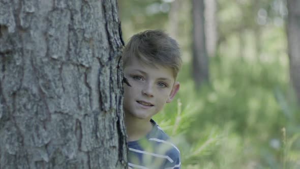 Boy peeking around tree trunk
