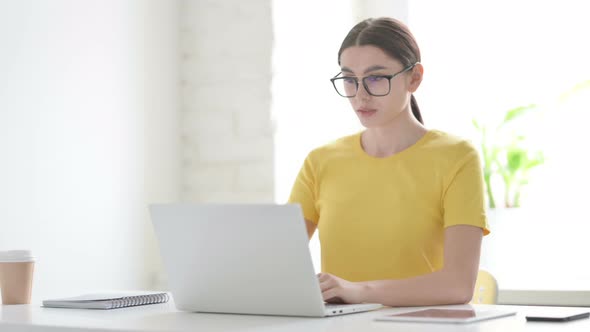 Woman Looking at Camera while using Laptop in Office