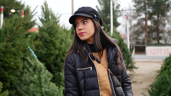 A beautiful hispanic woman shopping on a Christmas tree lot with green douglas fir conifers in a hol