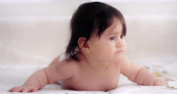 Cute Baby is Lying in a Diaper on Her Stomach on the Bed in the Nursery