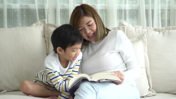 Asian Mother And Her Son Reading A Book On Sofa In Living Room Slow Motion