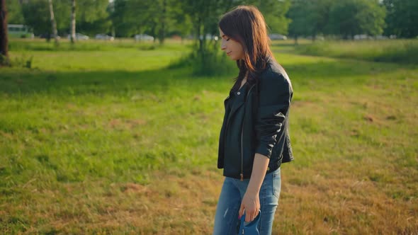 A Young Female in Jeans Leading Her Dog for a Walk in the Park on a Leash.