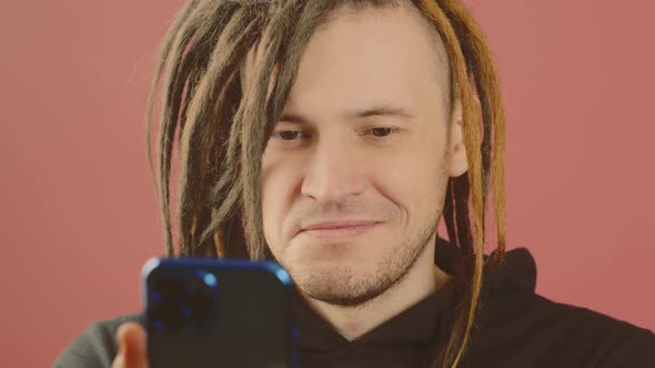 Young Happy Man Browsing Mobile Phone on Pink Background