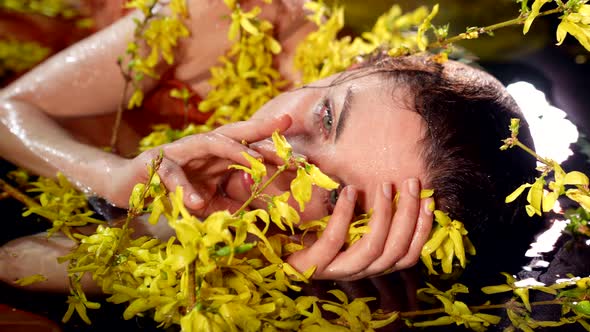 Romantic Female Portrait in Shallow of River or Lake Woman is Stroking Wet Yellow Flowers