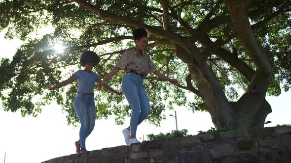 Two mixed race women walking on wall in park
