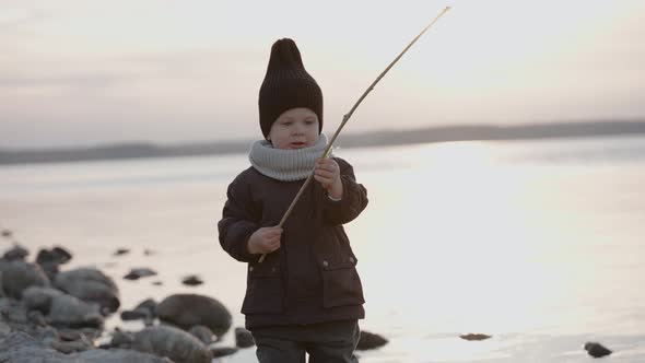 Baby Boy Walking on the Stone Shore Playing with Stick on an Autumn Evening