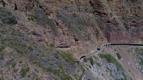 Drone panning shot of car driving on scenic coastal road cut out of cliff next to ocean - Chapman's