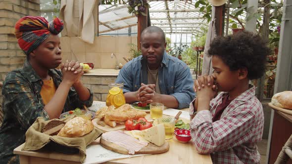 Afro-American Family Praying before Meal in Greenhouse