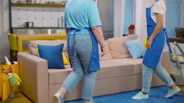 Happy and Tired Housewives in Apron Sitting on Couch and Giving High-five After Home Cleaning