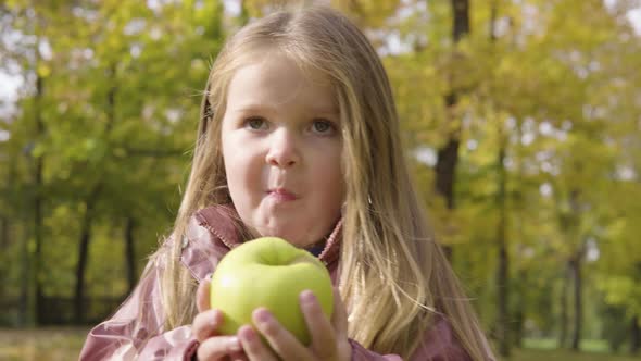 Cute Little Caucasian Girl Eats an Apple in a Park  Closeup