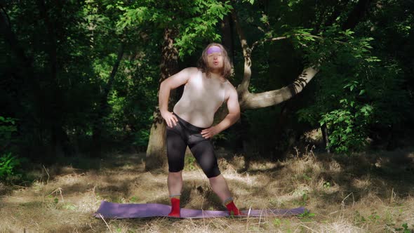 Expressive Overweight Man with Long Hair in Funny Female Clothes Doing Fitness in the Forest