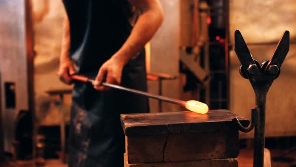 Mid section of glassblower shaping a molten glass