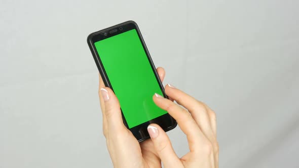 Wellgroomed Neat Female Hands with a Beautiful Manicure Hold a Black Smartphone with a Green Screen