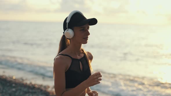 A Young Woman Runner is Listening to Music in Earphones and Training By a Sea