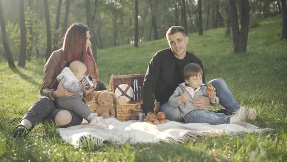 Wide Shot Portrait of Happy Relaxed Young Family Posing in Sunlight on Summer Picnic Outdoors