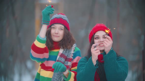 Two Young Smiling Women Playing at Winter with Lighted Up Sparklers and Looking Into Camera