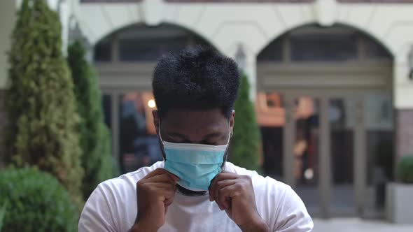 Portrait of a Young African American Man Looking at the Camera and Putting on a Protective Medical