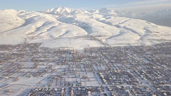 Smooth Mountains Covered With Snow And Town With Small Buildings