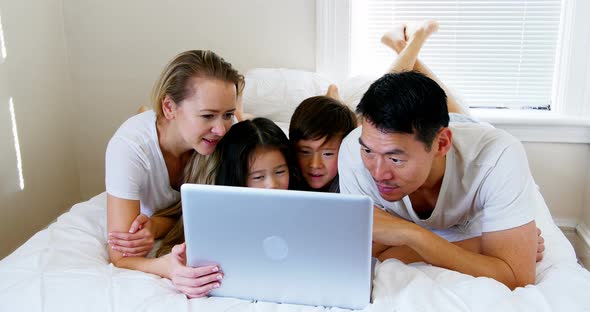 Happy family relaxing on bed and using laptop