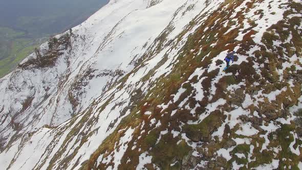 Aerial view of a trail runner running up the ridge of a snowy mountain