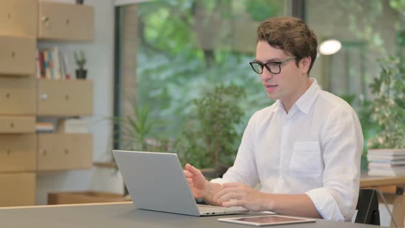 Young Man Celebrating Success While Using Laptop in Modern Office